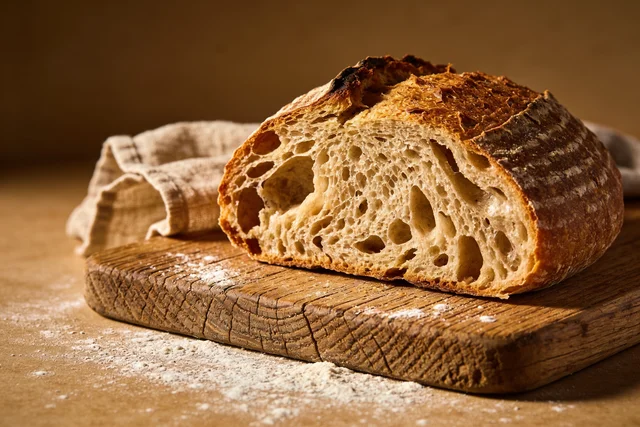 Seedream 4.5: Artisan sourdough loaf on a rustic wooden board, flour dust, torn crumb showing open holey