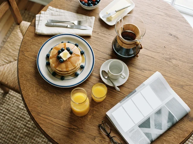 Nano Banana 2 Lite: Overhead breakfast scene: stack of pancakes with butter, glass pot of coffee, small juice 